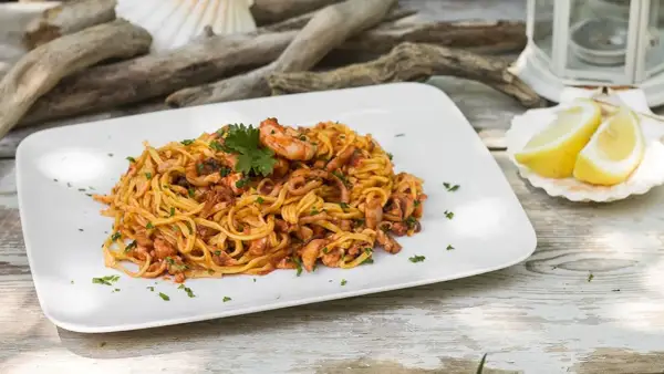 Un piatto di linguine al ragù di pesce, con gamberi e calamari, guarnito con prezzemolo e spicchi di limone su una conchiglia.