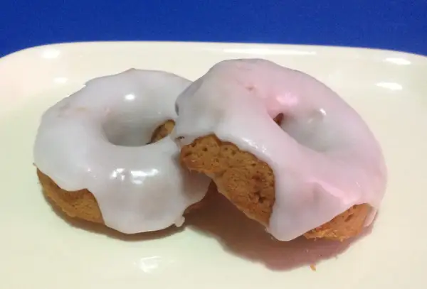 Due ciambelle con glassa per biscotti che si asciuga subito, su un piatto bianco.