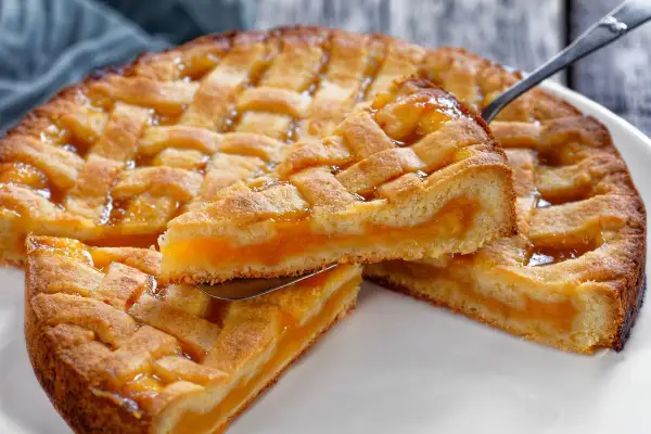 Deliziosa crostata senza glutine con ripieno di albicocche, la fetta sollevata mostra la morbidezza dell'impasto e la succosità della frutta.