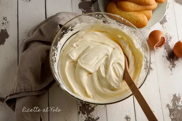 Una ciotola di soffice crema al mascarpone, pronta per preparare un delizioso tiramisù. Accanto, savoiardi e gusci d'uovo.