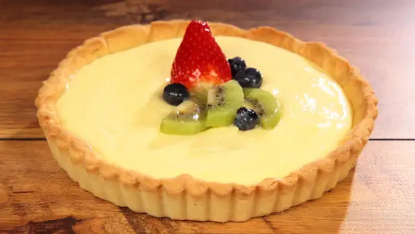 Deliziosa crostata con crema pasticcera, guarnita con fragola, kiwi e mirtilli. Un dolce invitante su un tavolo di legno.