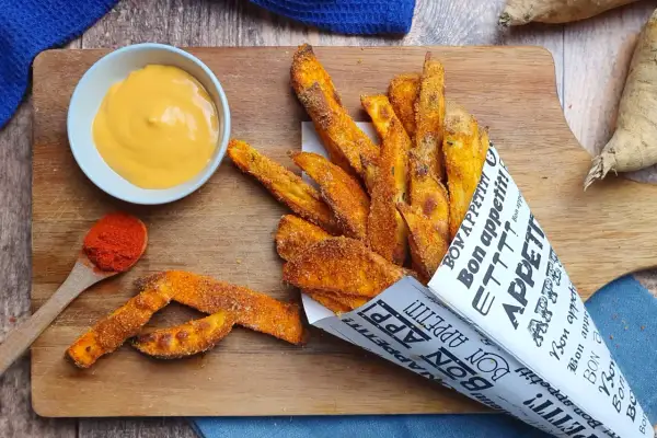 Patate dolci fritte croccanti, servite in un cono di carta con la scritta "Bon appétit!", accompagnate da una salsa cremosa e paprika.