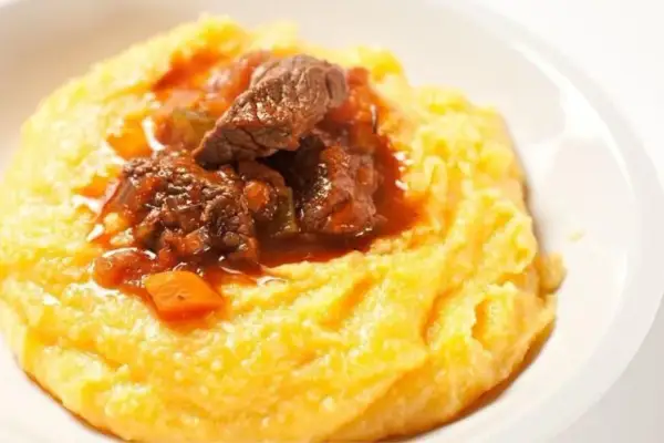 Un invitante spezzatino con piselli, servito su un letto di morbida polenta gialla. Un piatto confortante e saporito.
