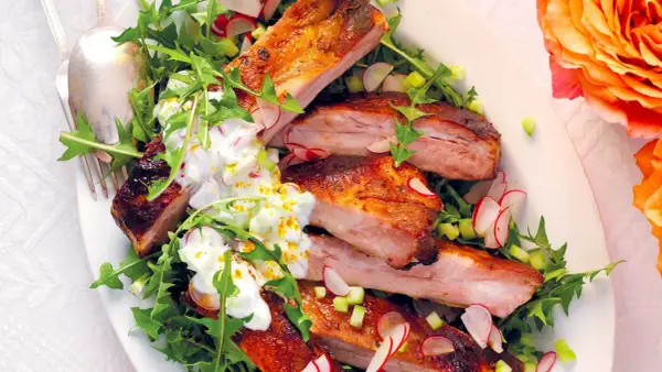 Costine di maiale succulente, perfette per una marinatura saporita, servite su un letto di rucola e ravanelli, con una salsa cremosa.