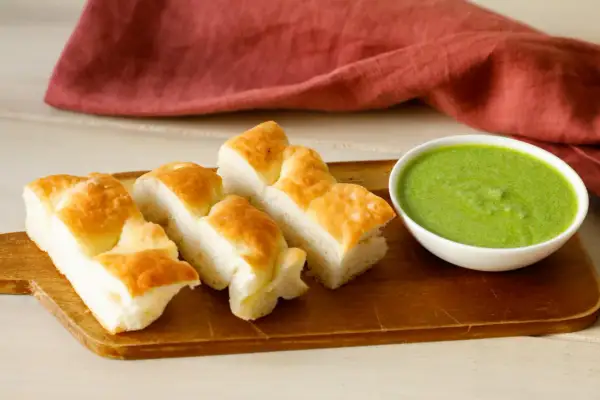 Focaccia tagliata a pezzi su tagliere di legno, accanto una ciotolina con pesto di salvia.