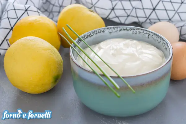 Una ciotola di cremosa maionese allo yogurt, guarnita con erba cipollina, accanto a limoni freschi e uova.