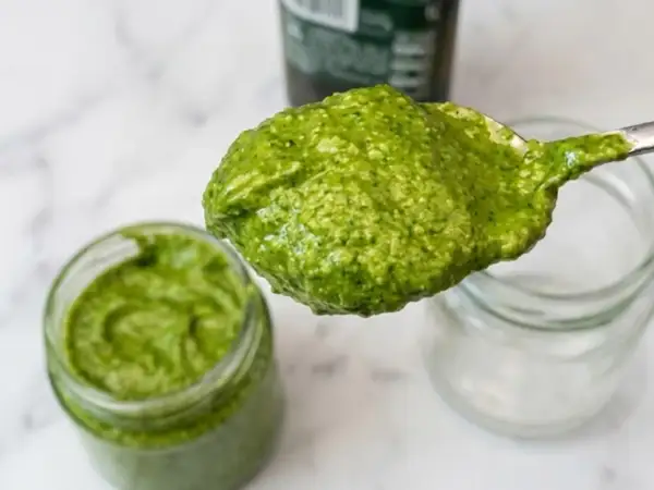 Un cucchiaio pieno di pesto fatto in casa, verde brillante, pronto per essere gustato.